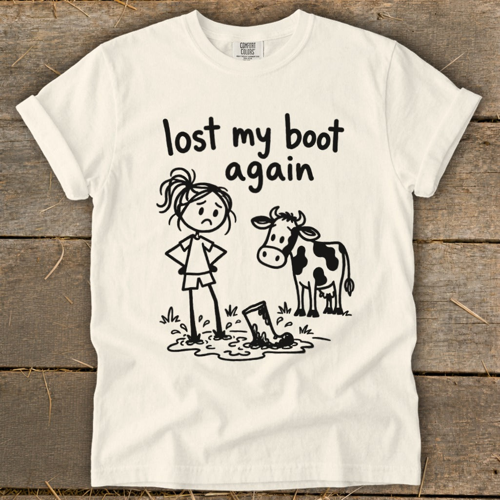 Off-white t-shirt with a humorous stick figure design featuring a girl, a cow, and text reading lost my boot again.