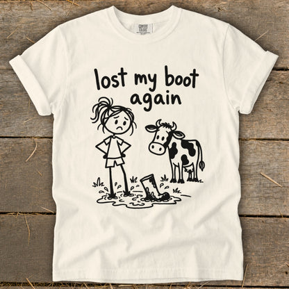 Off-white t-shirt with a humorous stick figure design featuring a girl, a cow, and text reading lost my boot again.