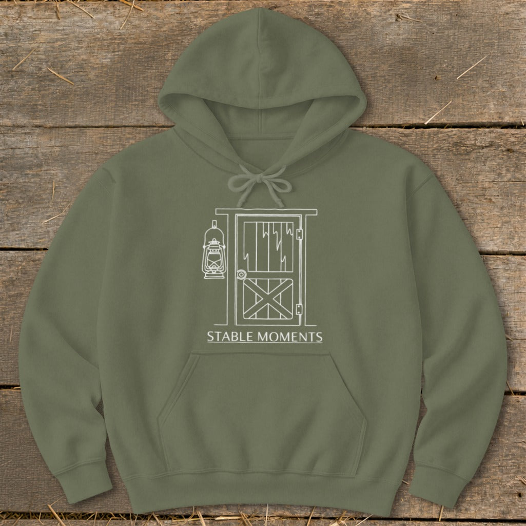 Olive green hoodie with white line art of a barn door and lantern, text says "STABLE MOMENTS".
