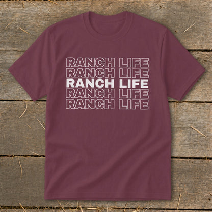 Maroon short-sleeved t-shirt with five rows of stacked white text that reads RANCH LIFE, laid flat on rustic wood.