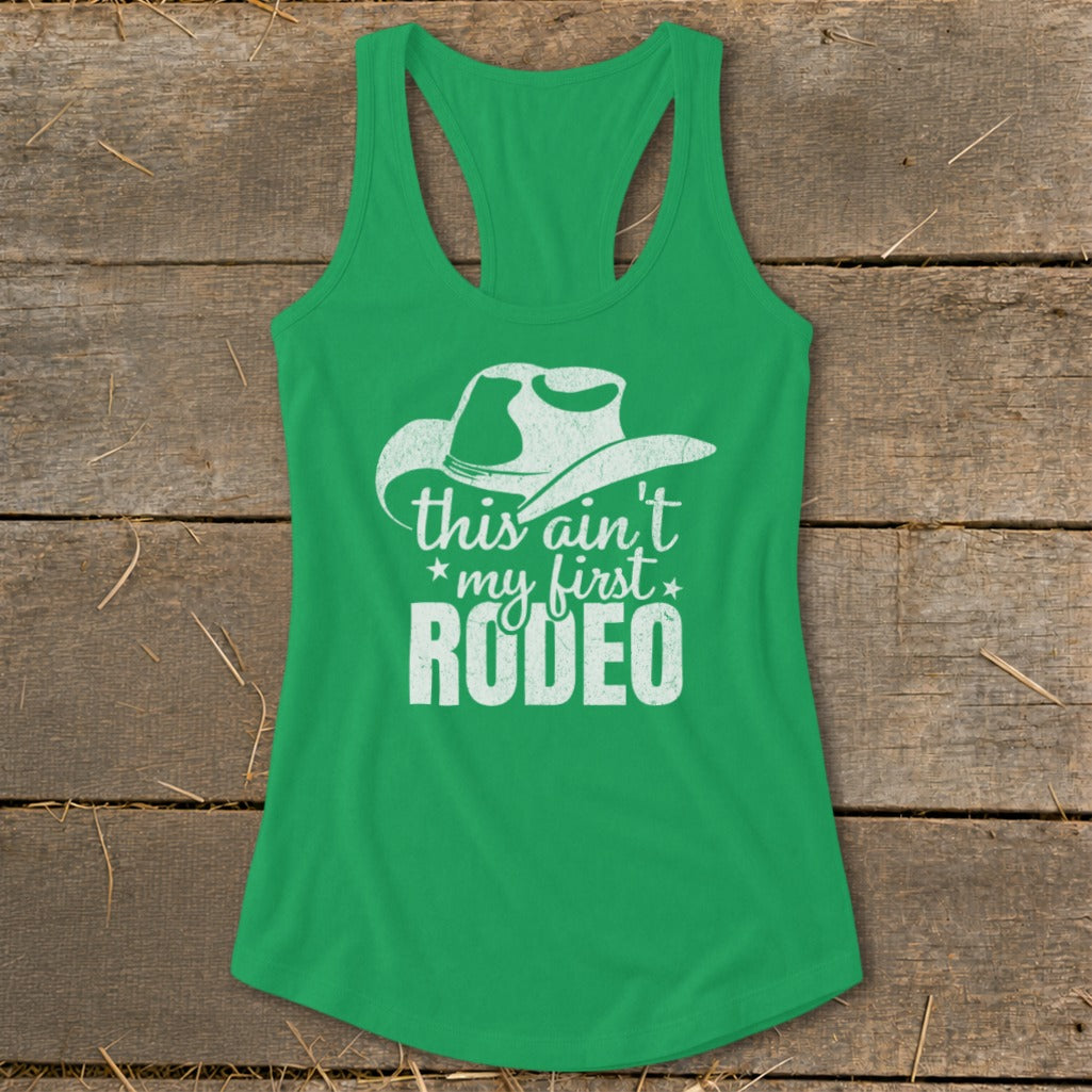 Green tank top with white text and cowboy hat graphic that reads "this ain't my first RODEO".