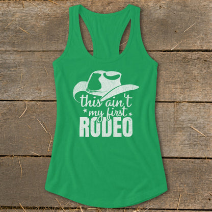 Green tank top with white text and cowboy hat graphic that reads "this ain't my first RODEO".