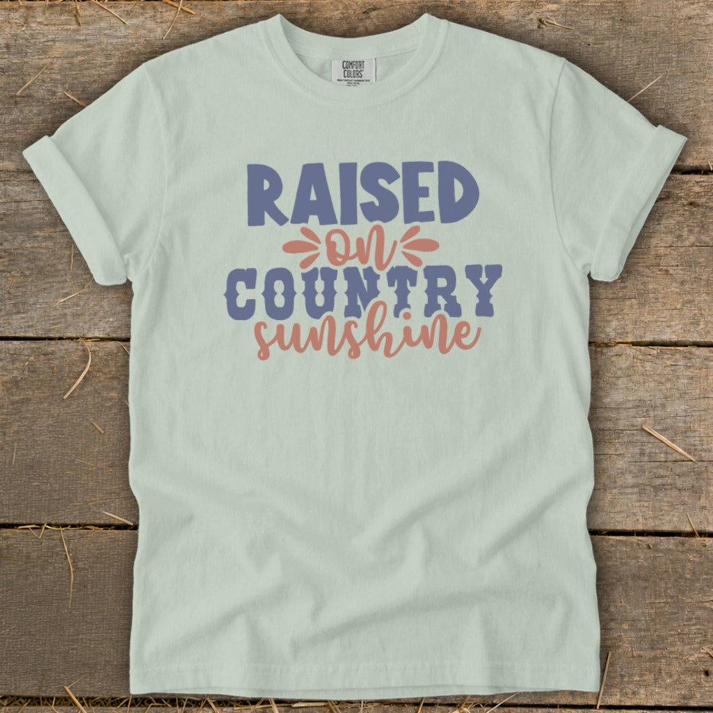 Light green t-shirt with "Raised on Country Sunshine" text in blue and coral.