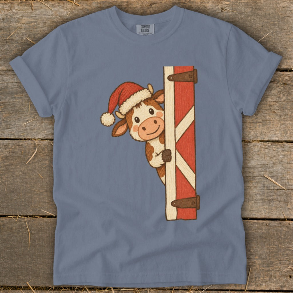 Cow wearing Santa hat peeking from behind a barn door.