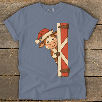 Cow wearing Santa hat peeking from behind a barn door.