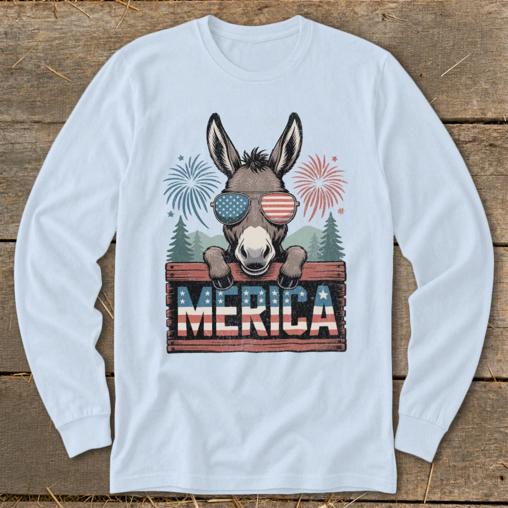 Donkey wearing American flag sunglasses peeking over "MERICA" sign with fireworks.