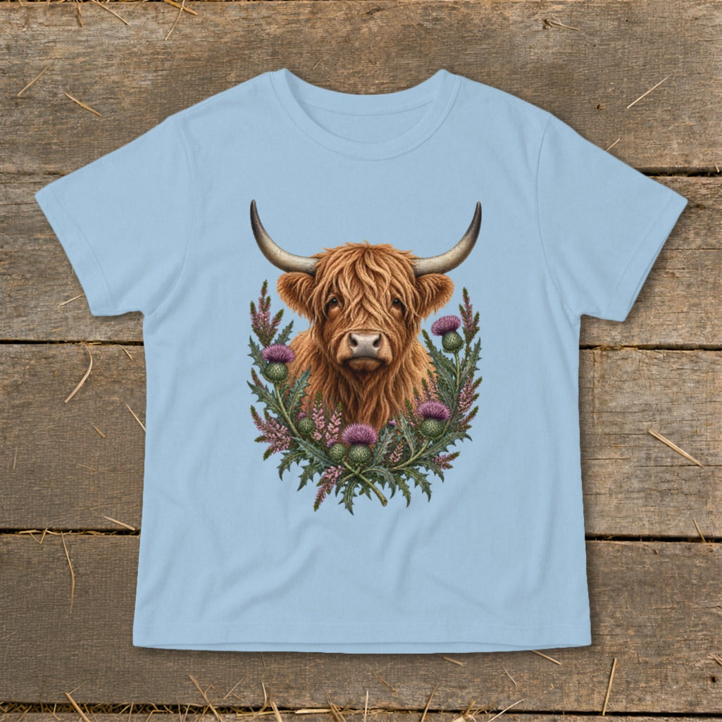 Highland cow portrait surrounded by thistles on a light blue t-shirt.