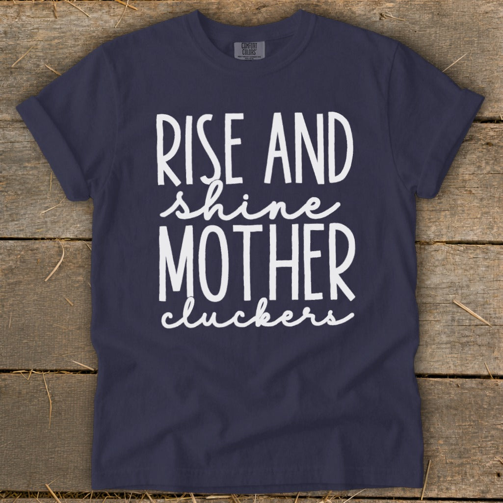 Navy t-shirt with "Rise and shine mother cluckers" text in white cursive.