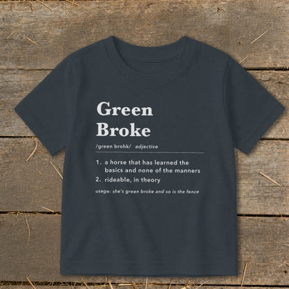 Dark gray short-sleeved children's t-shirt printed with a humorous definition of Green Broke against a rustic wooden background.