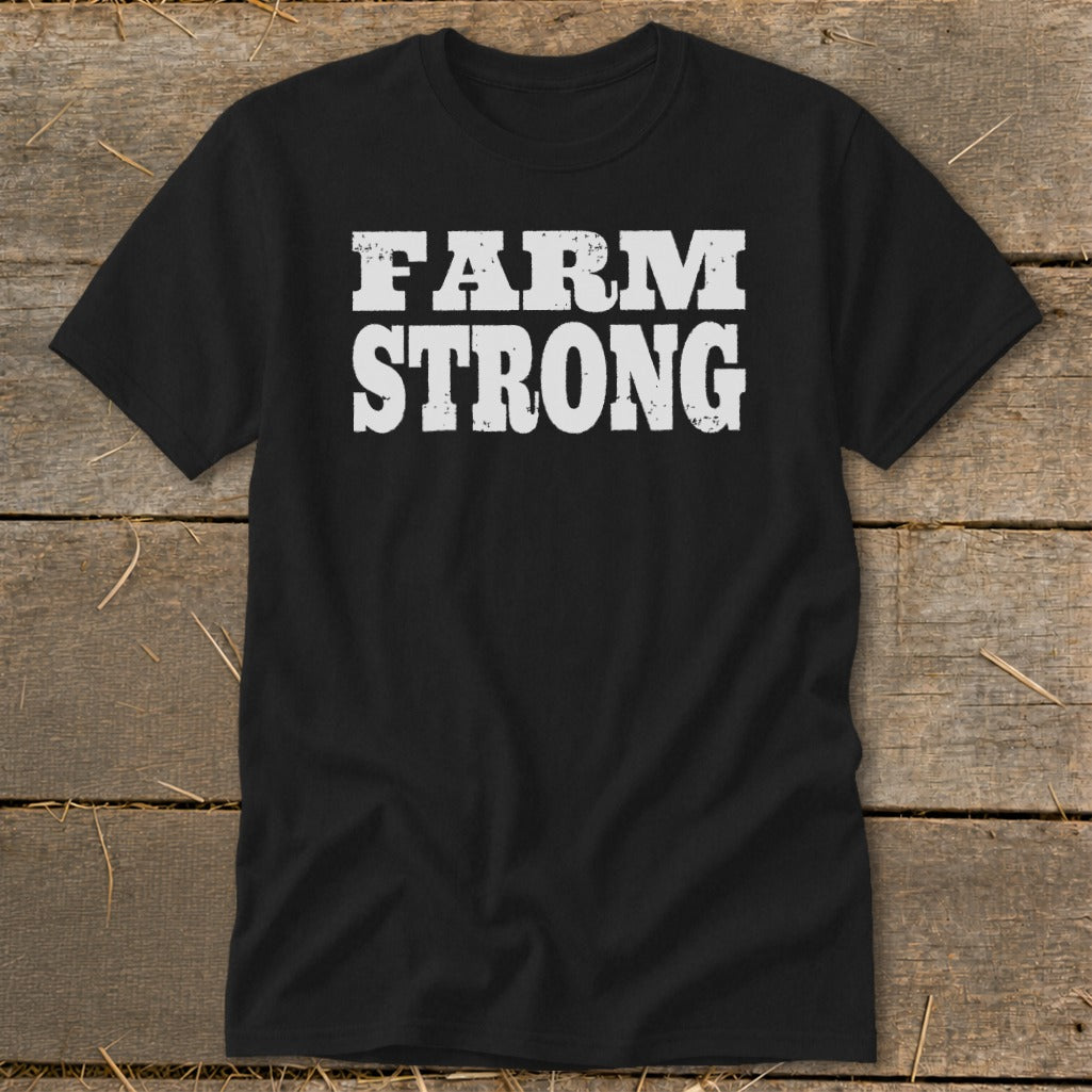 A black t-shirt with the distressed white text FARM STRONG laid flat on a wooden surface.