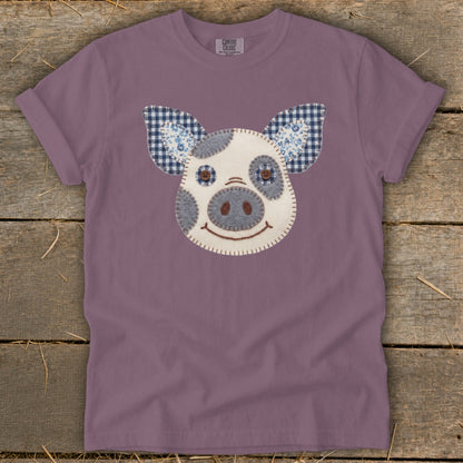 Purple t-shirt with a stitched appliqué of a pig's face and ears.