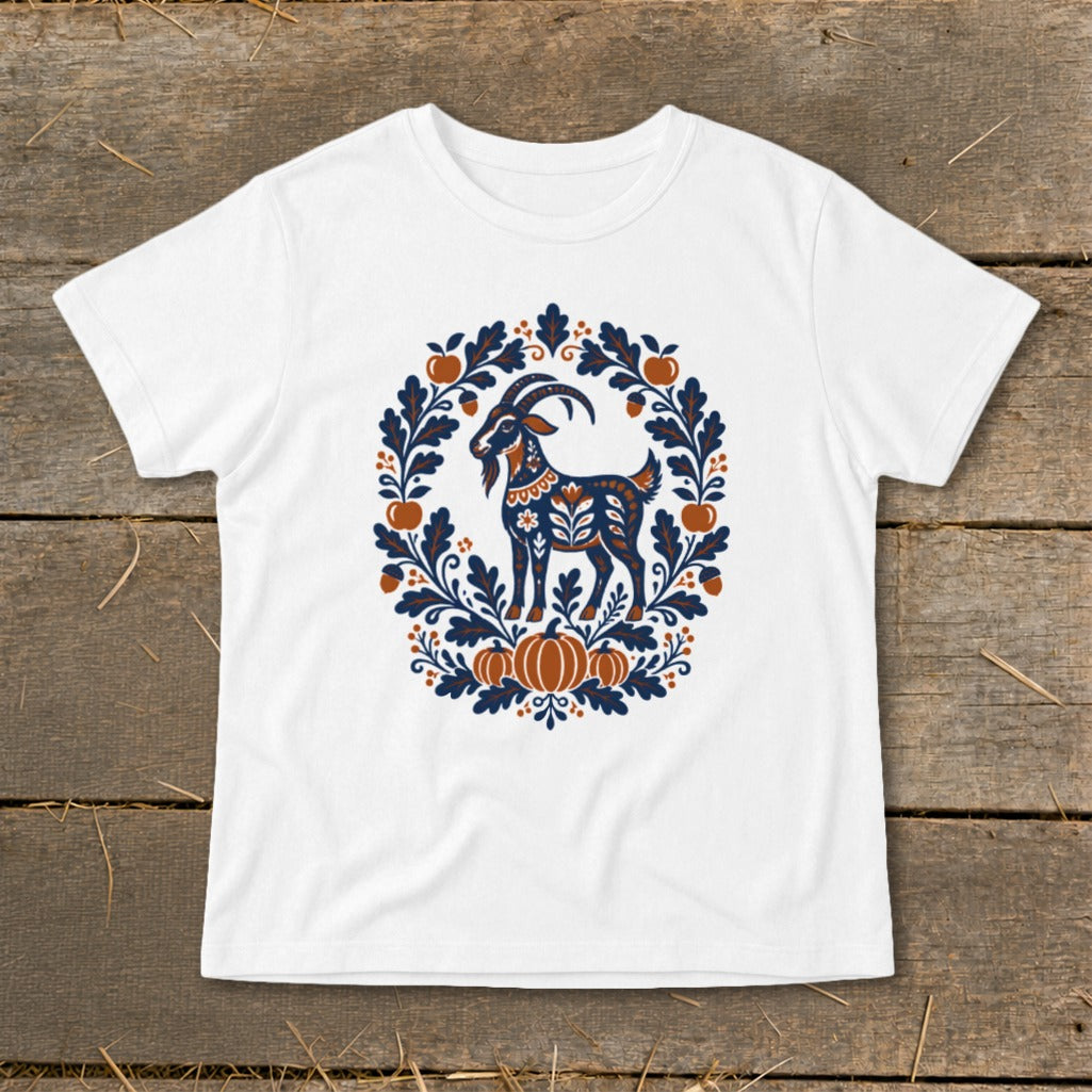 A white t-shirt featuring a folk art graphic of a goat surrounded by leaves, acorns, and pumpkins on a wooden background.