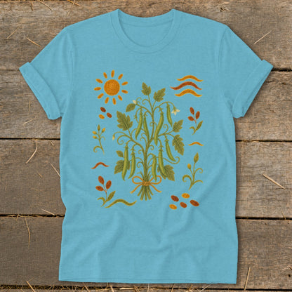 Light blue t-shirt with a detailed illustration of a pea plant with pods, sun, and leaves.