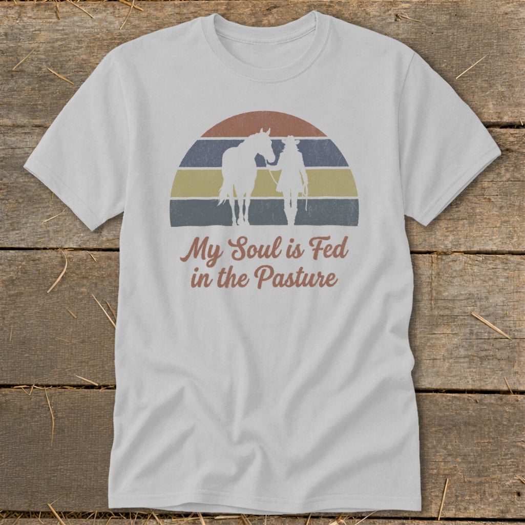 White t-shirt with vintage sunset design of person and horse with text "My Soul is Fed in the Pasture".