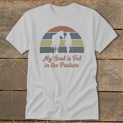 White t-shirt with vintage sunset design of person and horse with text "My Soul is Fed in the Pasture".