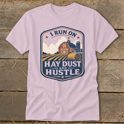 Pink t-shirt with a farm scene and "I Run On Hay Dust And Hustle" text.
