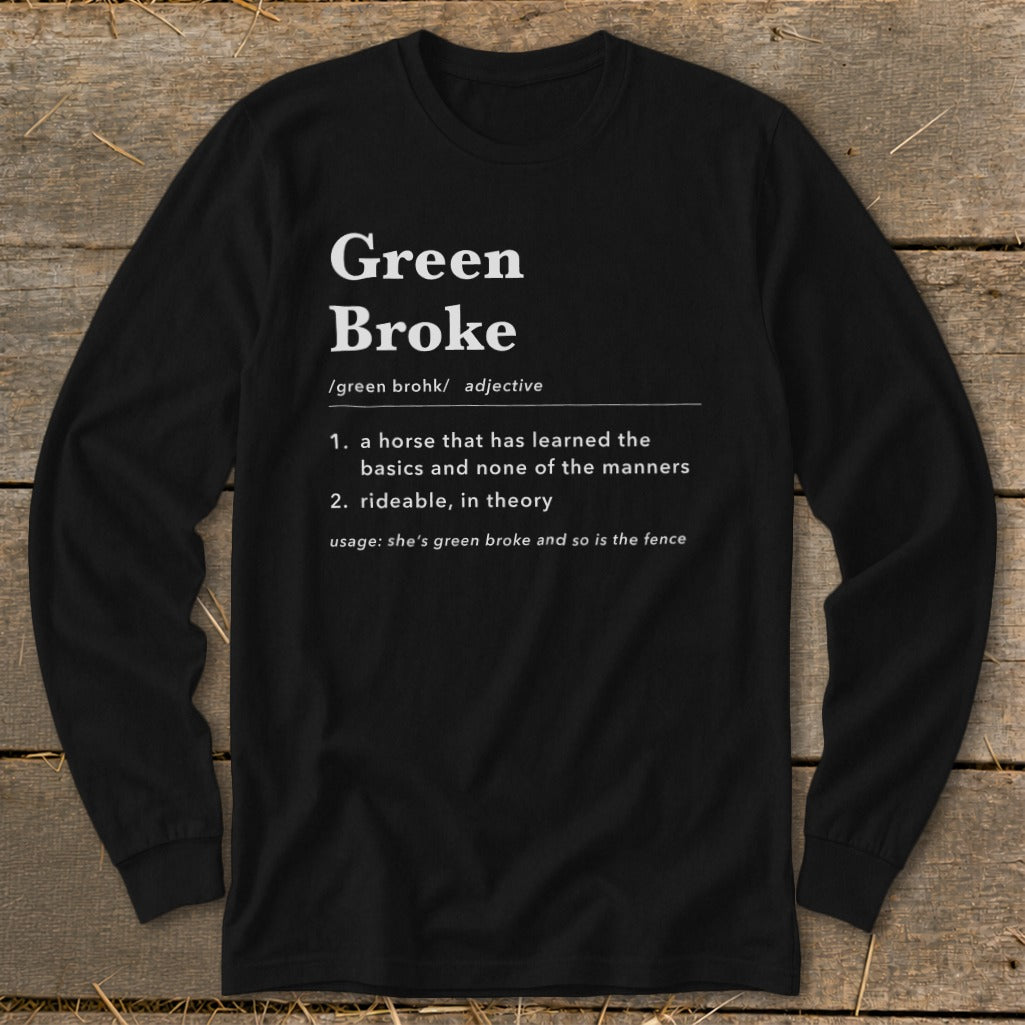 Black long-sleeve t-shirt with white text defining green broke on a rustic wooden background.
