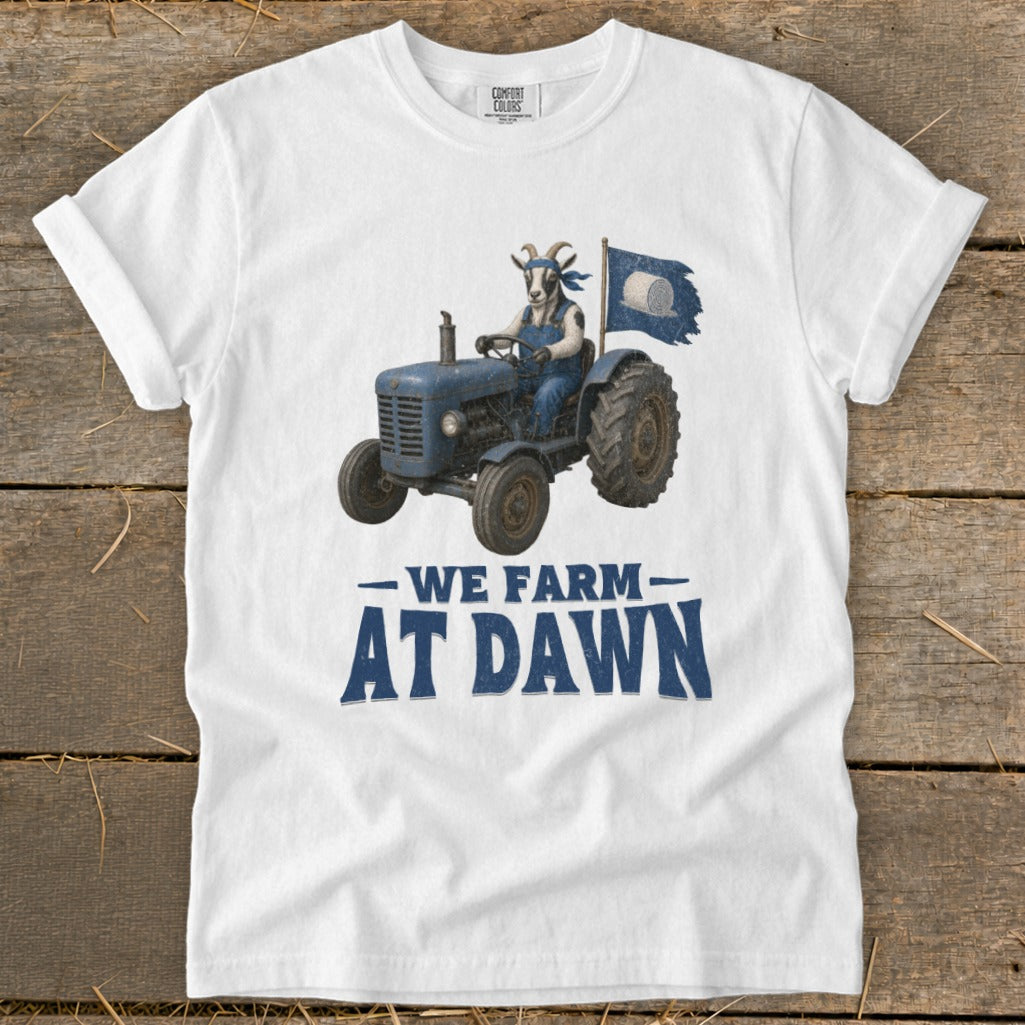 White t-shirt with graphic of goat driving tractor and "WE FARM AT DAWN" text.