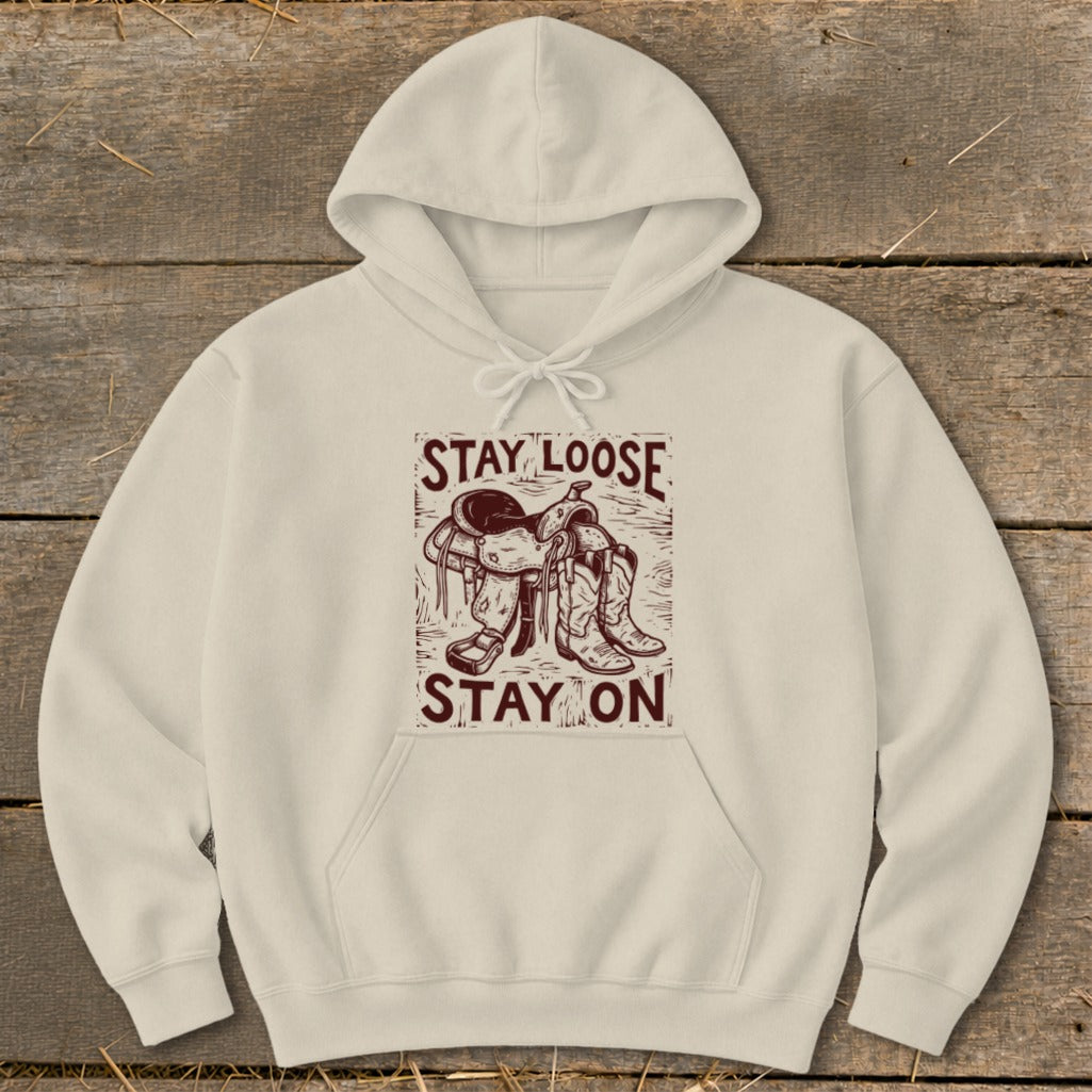 Cream hoodie with a graphic of a saddle and boots and text "STAY LOOSE STAY ON".