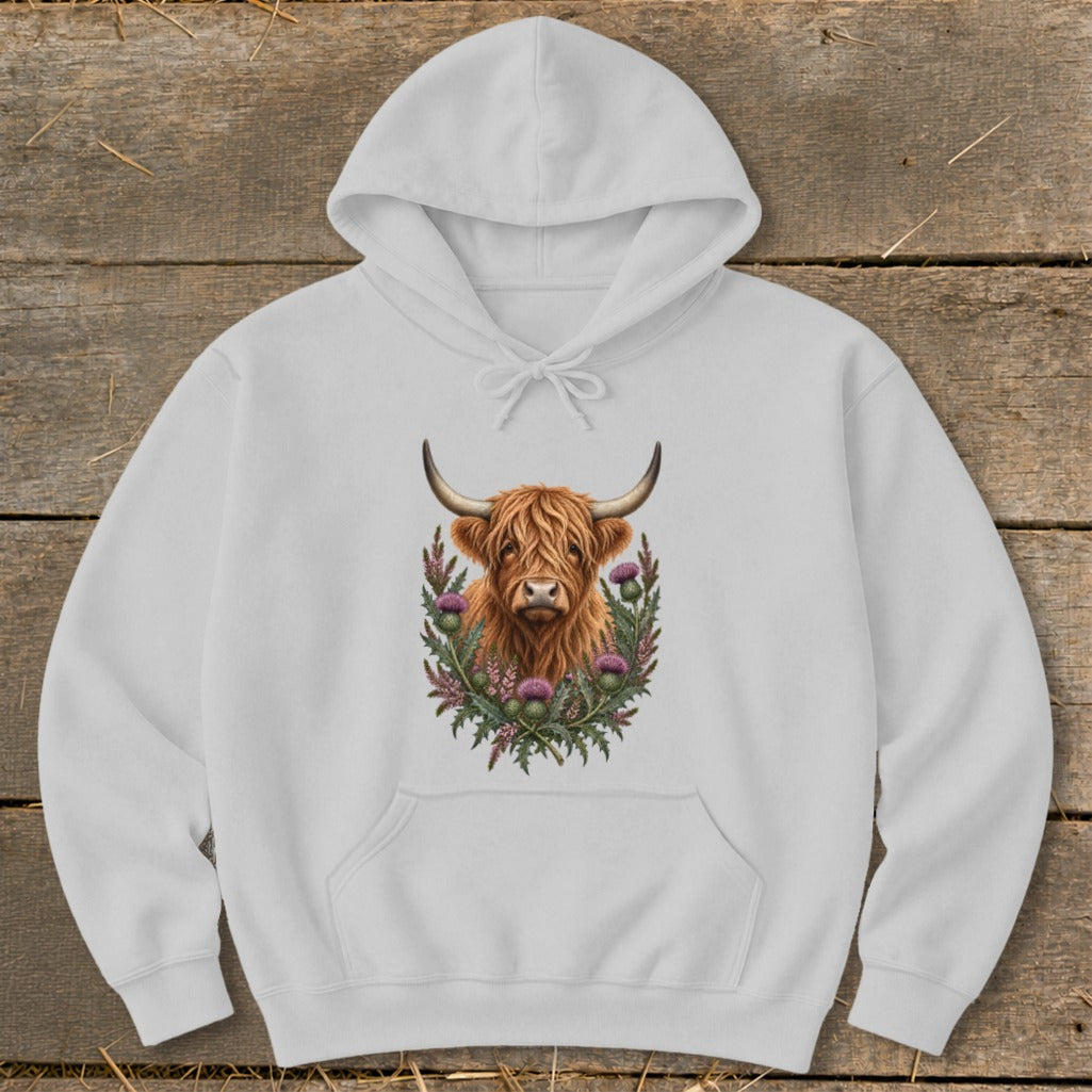 White hoodie with a highland cow illustration surrounded by thistles.
