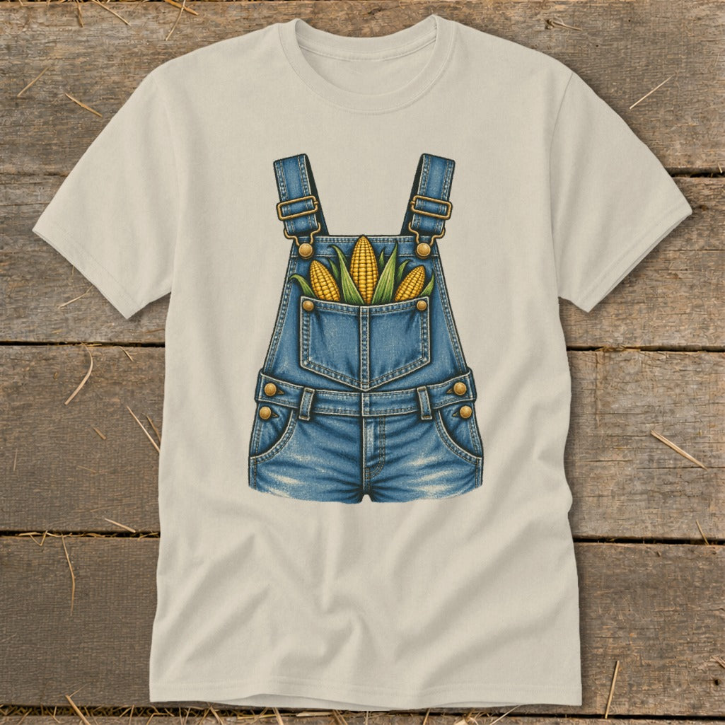 Cream t-shirt with graphic of denim overalls and three ears of corn in pocket.