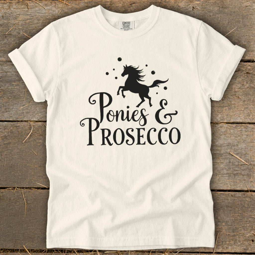 White t-shirt with black graphic of a jumping horse and text "Ponies & Prosecco".