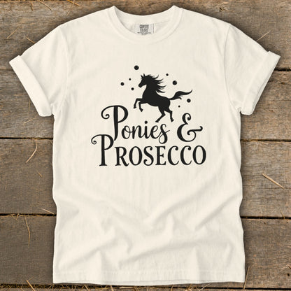 White t-shirt with black graphic of a jumping horse and text "Ponies & Prosecco".