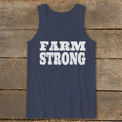 A navy blue tank top featuring the white distressed text FARM STRONG centered on a rustic wooden background.