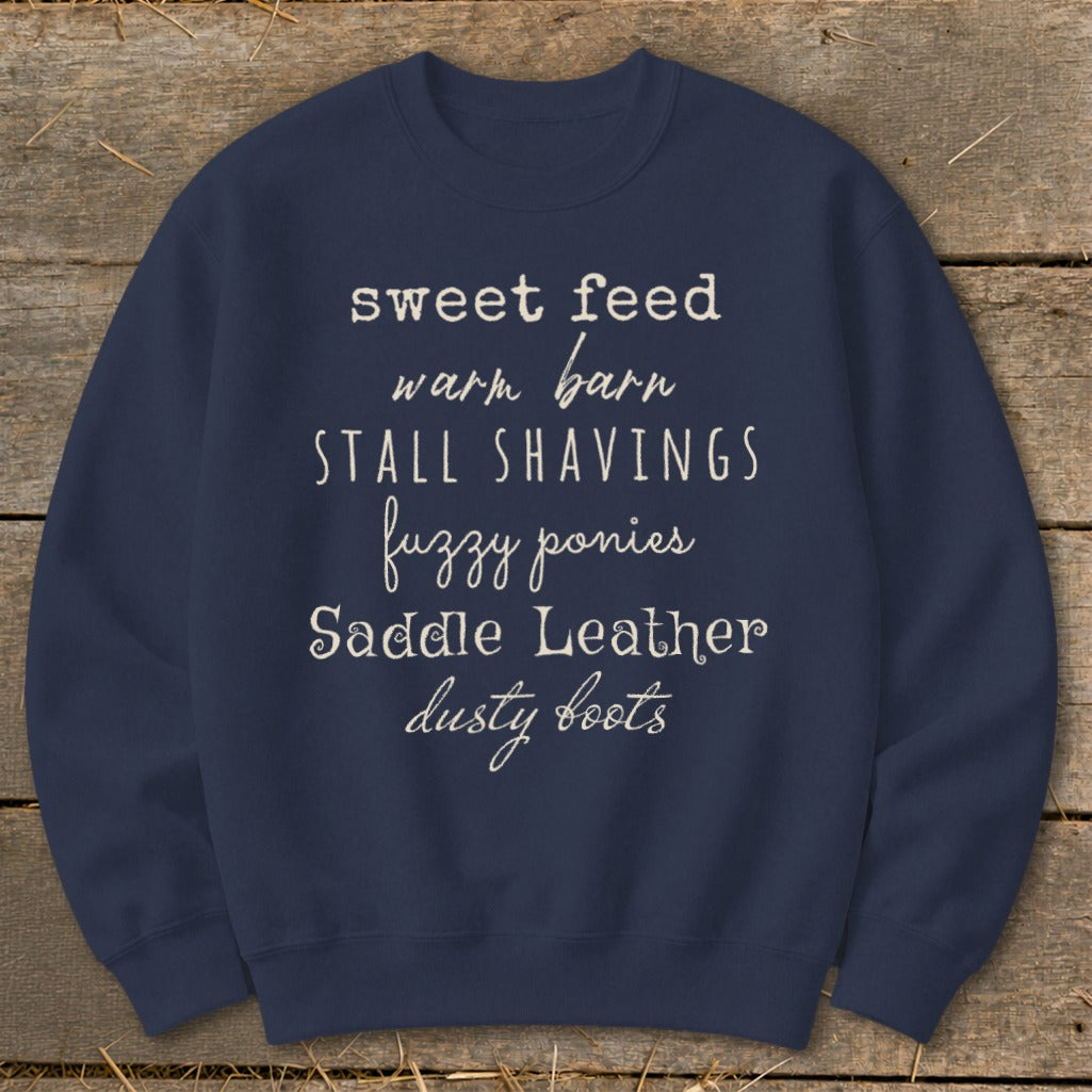 Navy sweatshirt with white text listing "sweet feed, warm barn, stall shavings, fuzzy ponies, saddle leather, dusty boots".