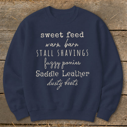 Navy sweatshirt with white text listing "sweet feed, warm barn, stall shavings, fuzzy ponies, saddle leather, dusty boots".