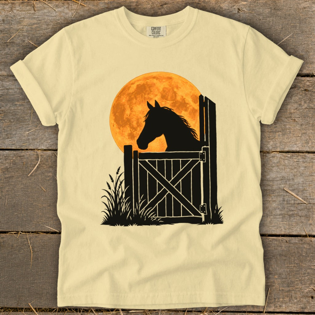 A pale yellow t-shirt features a black graphic of a horse looking over a gate against an orange moon.