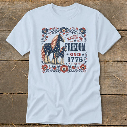 Light blue t-shirt with patriotic horses and "Raised on Freedom Since 1776" text.