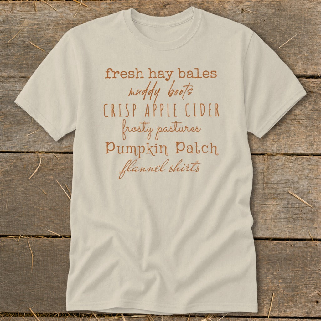 Light-colored t-shirt with text listing autumn activities: fresh hay bales, muddy boots, crisp apple cider.