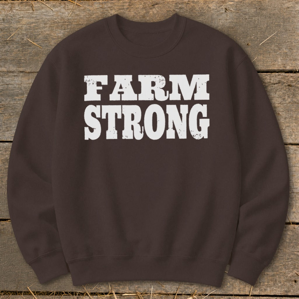 Dark brown crewneck sweatshirt featuring white distressed text that reads "FARM STRONG" on a rustic wooden background.