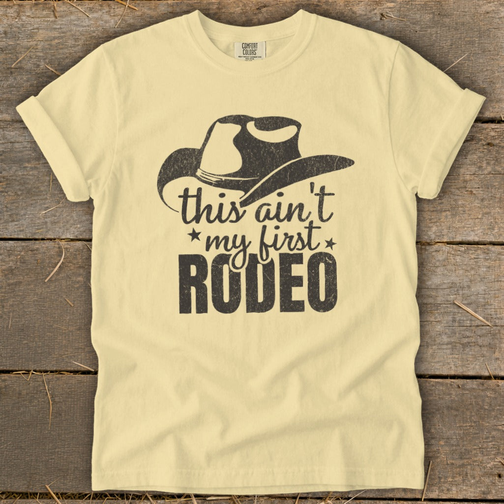 Light yellow t-shirt with cowboy hat graphic and text "this ain't my first RODEO".