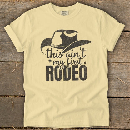 Light yellow t-shirt with cowboy hat graphic and text "this ain't my first RODEO".