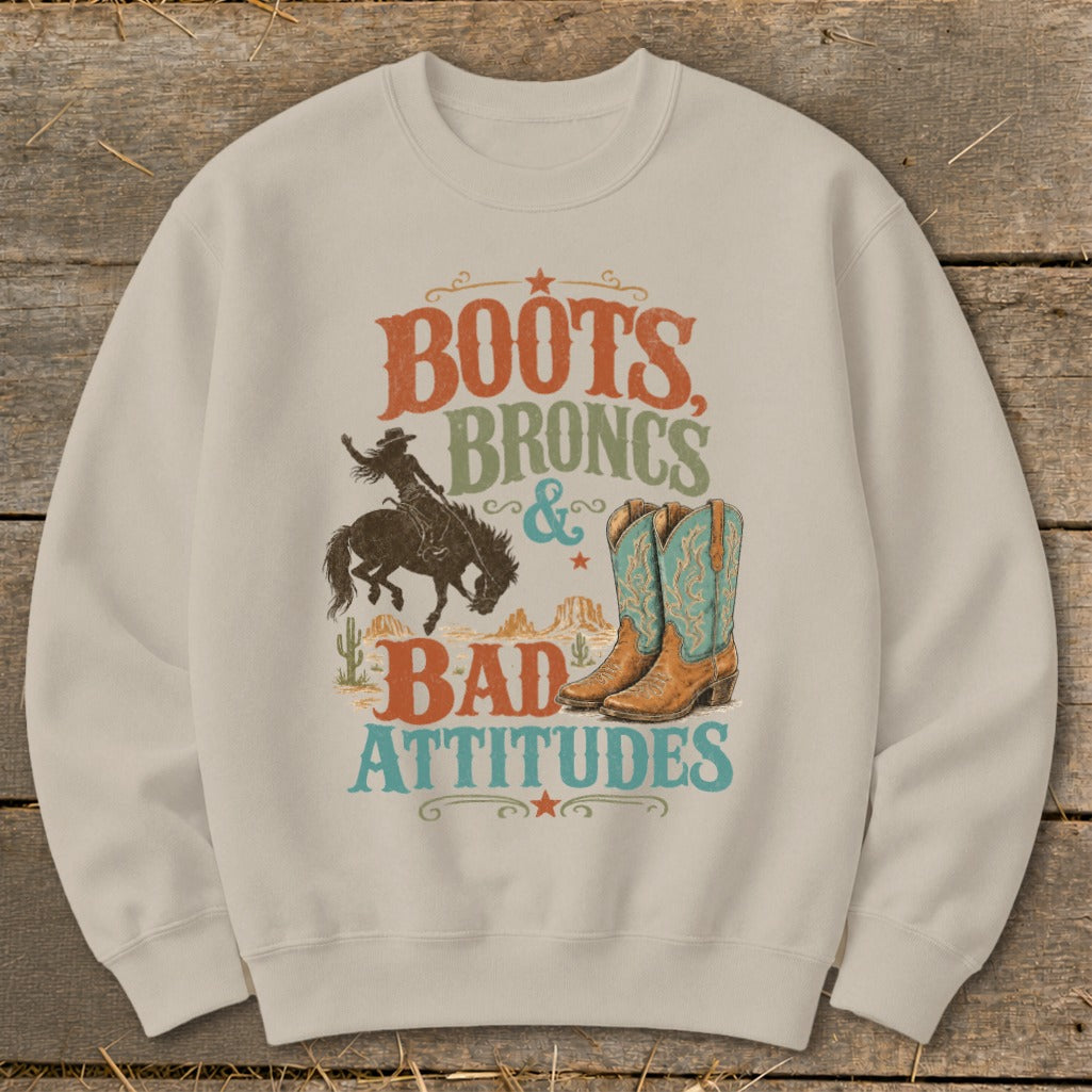 Cream sweatshirt with graphic "Boots, Broncs & Bad Attitudes" and cowboy imagery.
