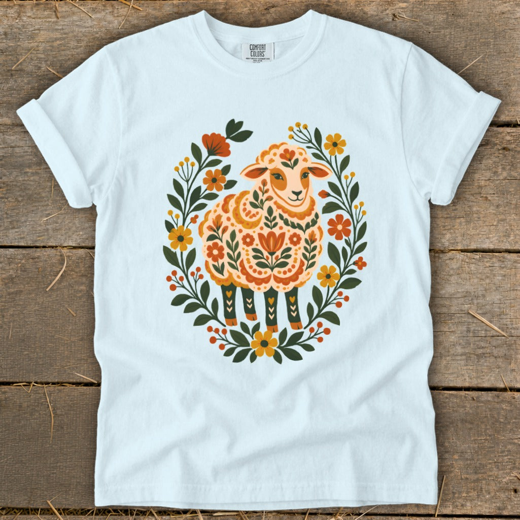 White t-shirt with a folk art sheep design surrounded by flowers.