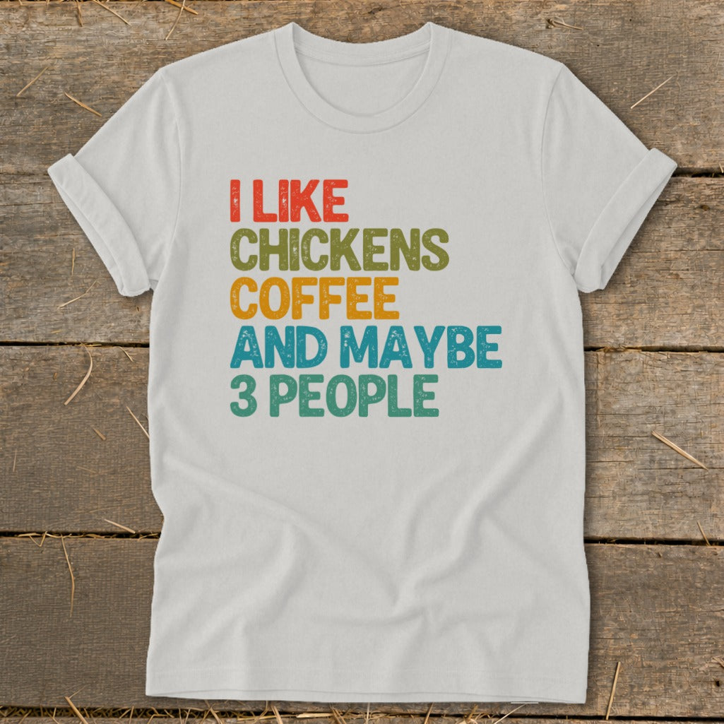 White t-shirt with text "I LIKE CHICKENS COFFEE AND MAYBE 3 PEOPLE" in retro colors.