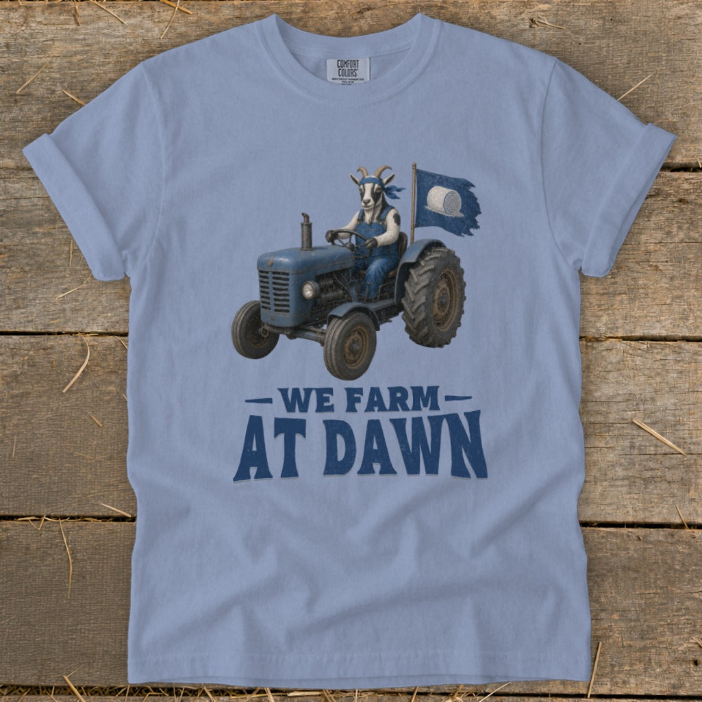 Goat in overalls drives tractor, waving flag with hay bale. Text "We Farm At Dawn."