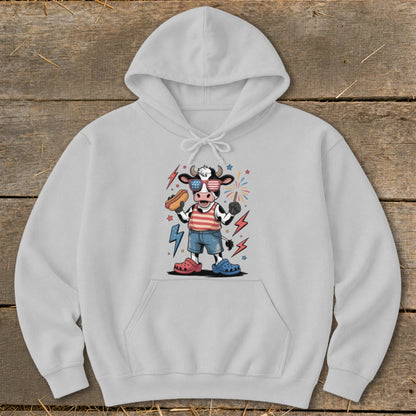 Cartoon cow in patriotic sunglasses holding a hot dog and a sparkler.