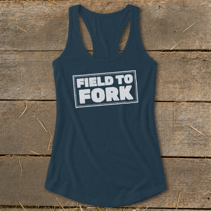 Dark blue racerback tank top featuring the white distressed text FIELD TO FORK laid out flat on a rustic wooden background.