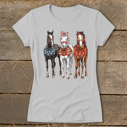 Three horses in patriotic bandanas and bows are printed on a light grey t-shirt.