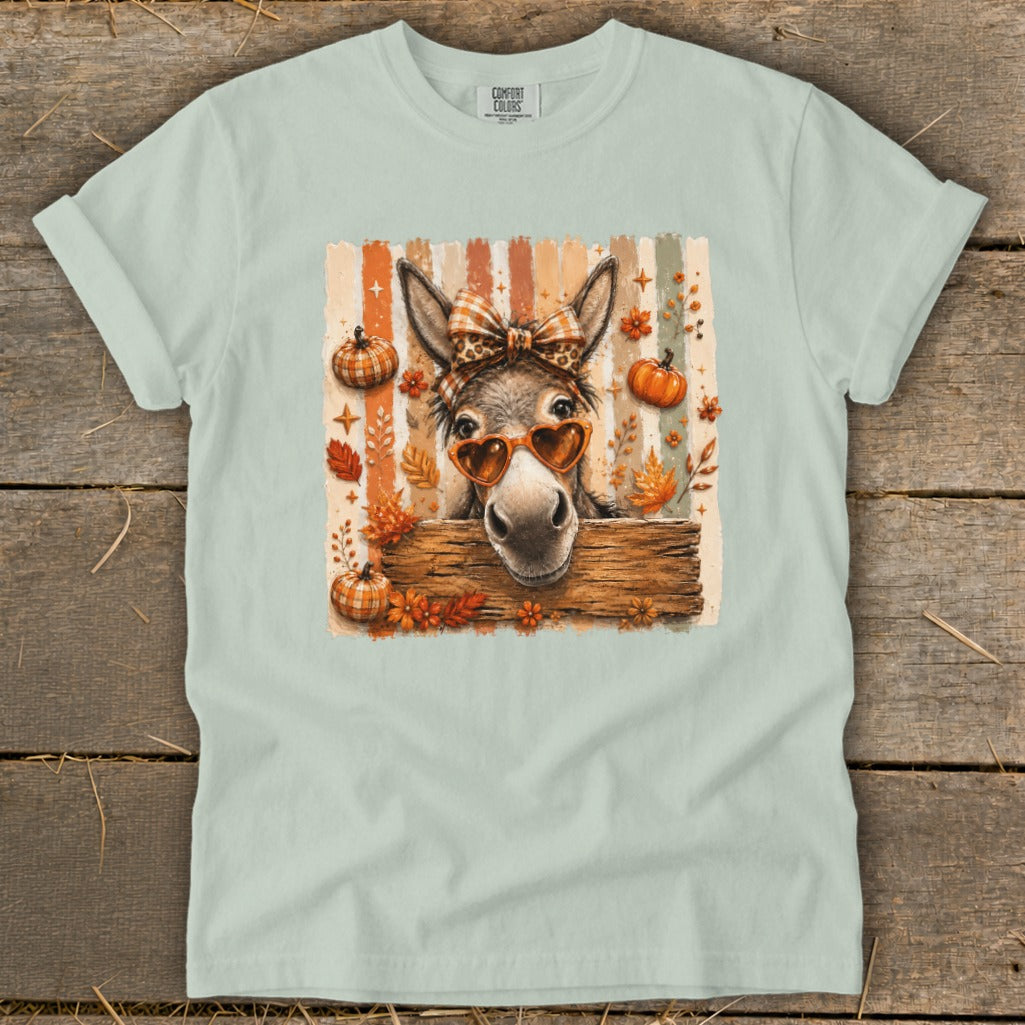 Donkey with heart sunglasses and bow, surrounded by pumpkins and autumn leaves.
