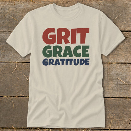 Light cream short-sleeved t-shirt with the stacked block text GRIT GRACE GRATITUDE in red, green, and blue.