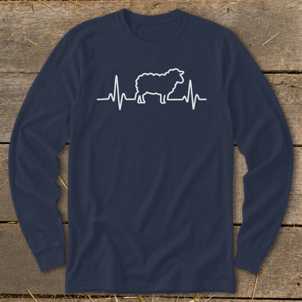 Navy blue long-sleeved t-shirt featuring a white heartbeat line graphic with a sheep silhouette in the center, displayed flat on a wooden background.