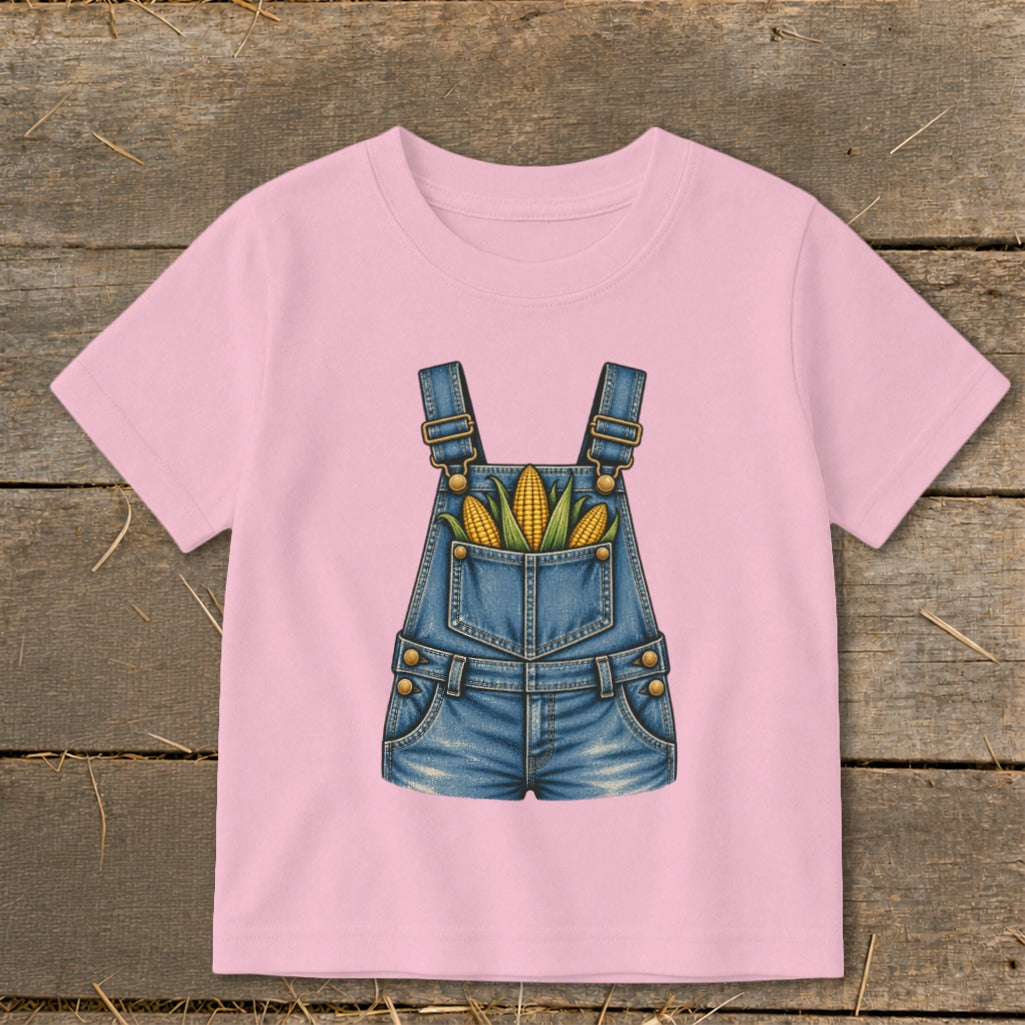 Pink t-shirt with a graphic of denim overalls filled with corn on the cob.