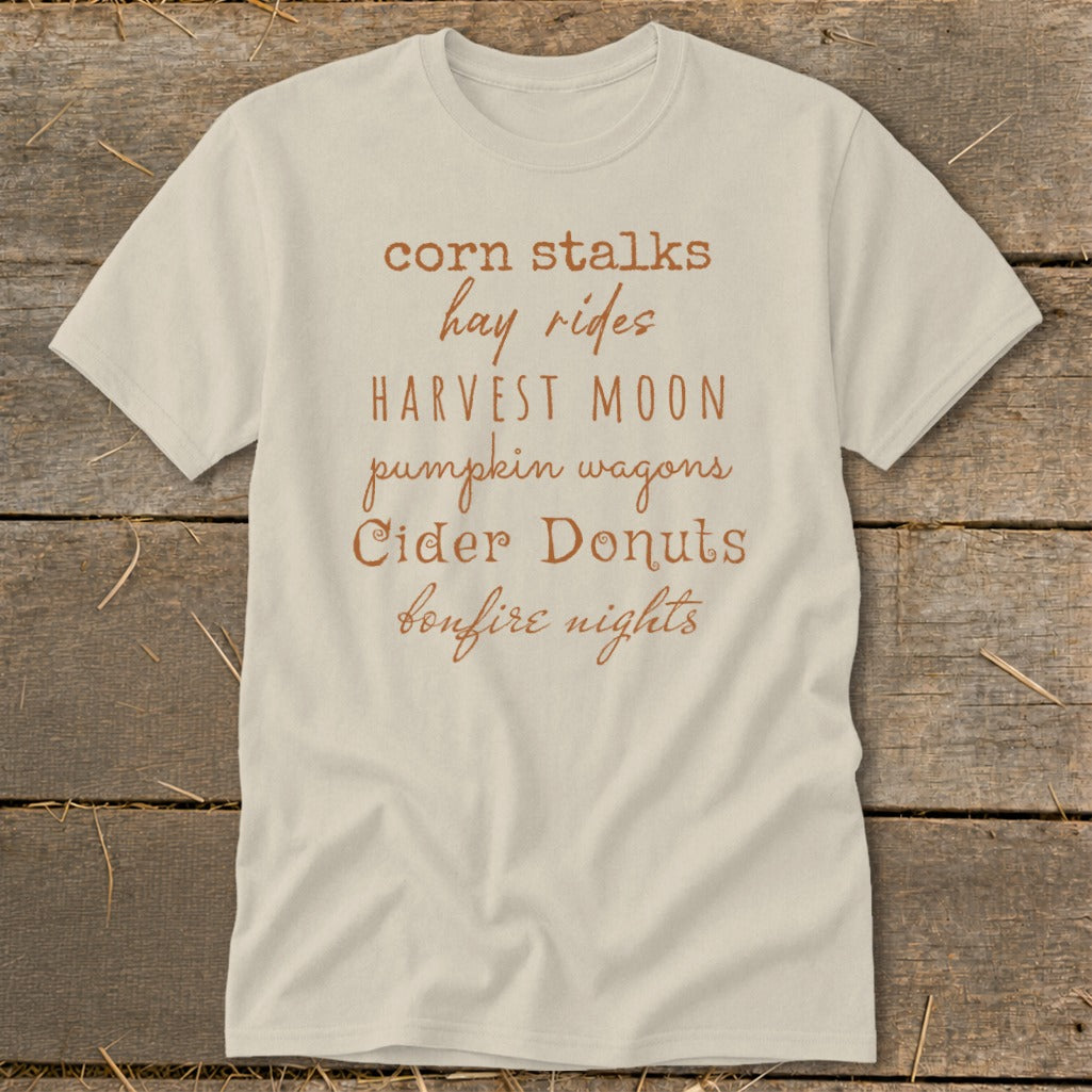 Cream t-shirt with brown text: corn stalks, hay rides, harvest moon, pumpkin wagons, cider donuts, bonfire nights.