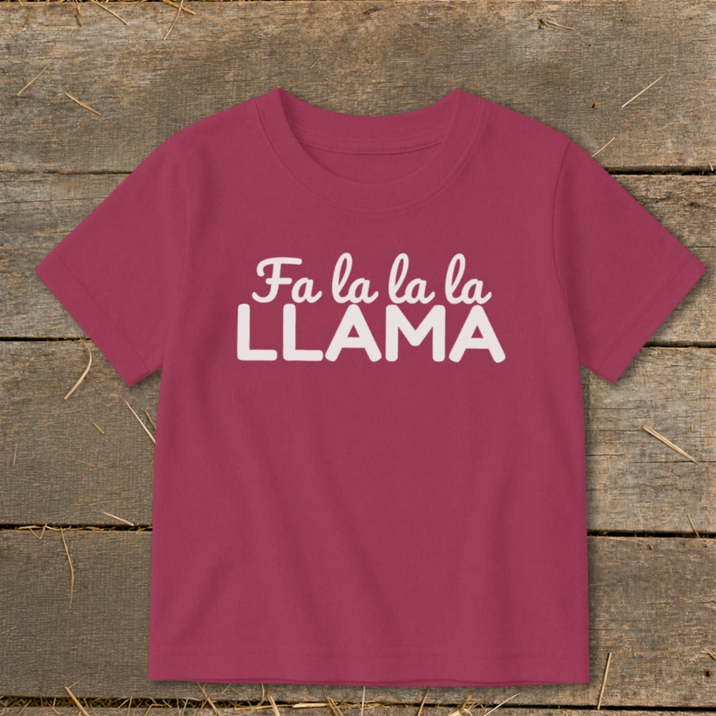 Magenta t-shirt with "Fa la la la LLAMA" text in white on a wooden background.