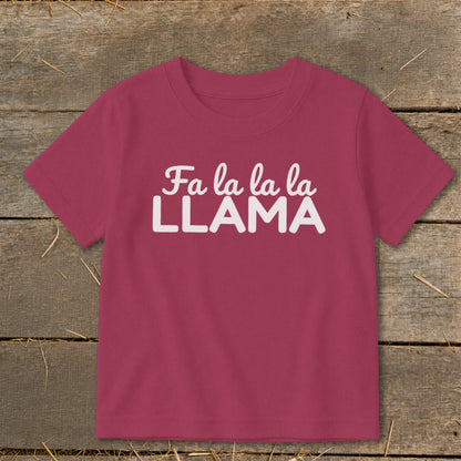 Magenta t-shirt with "Fa la la la LLAMA" text in white on a wooden background.